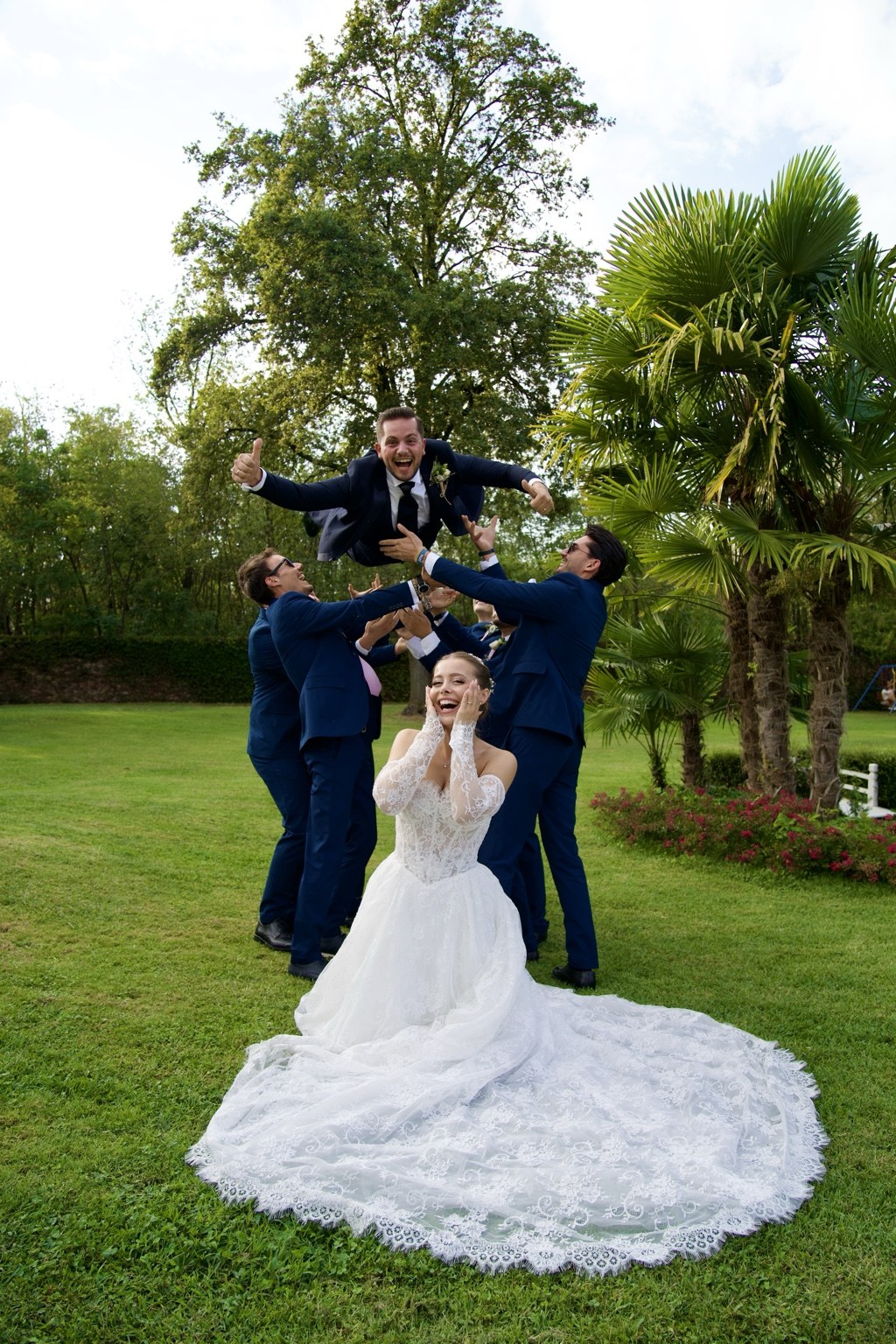 La sposa festeggia mentre gli amici sollevano lo sposo in giardino